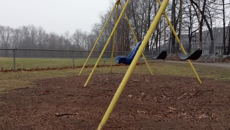 deserted playground swings swinging empty and lonely on a rainy and dreary day