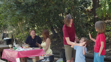 Tiro-Largo-De-Hermanos-Felices-Mirando-A-La-Cámara-Y-Dándose-Cinco-Durante-Un-Picnic-Familiar