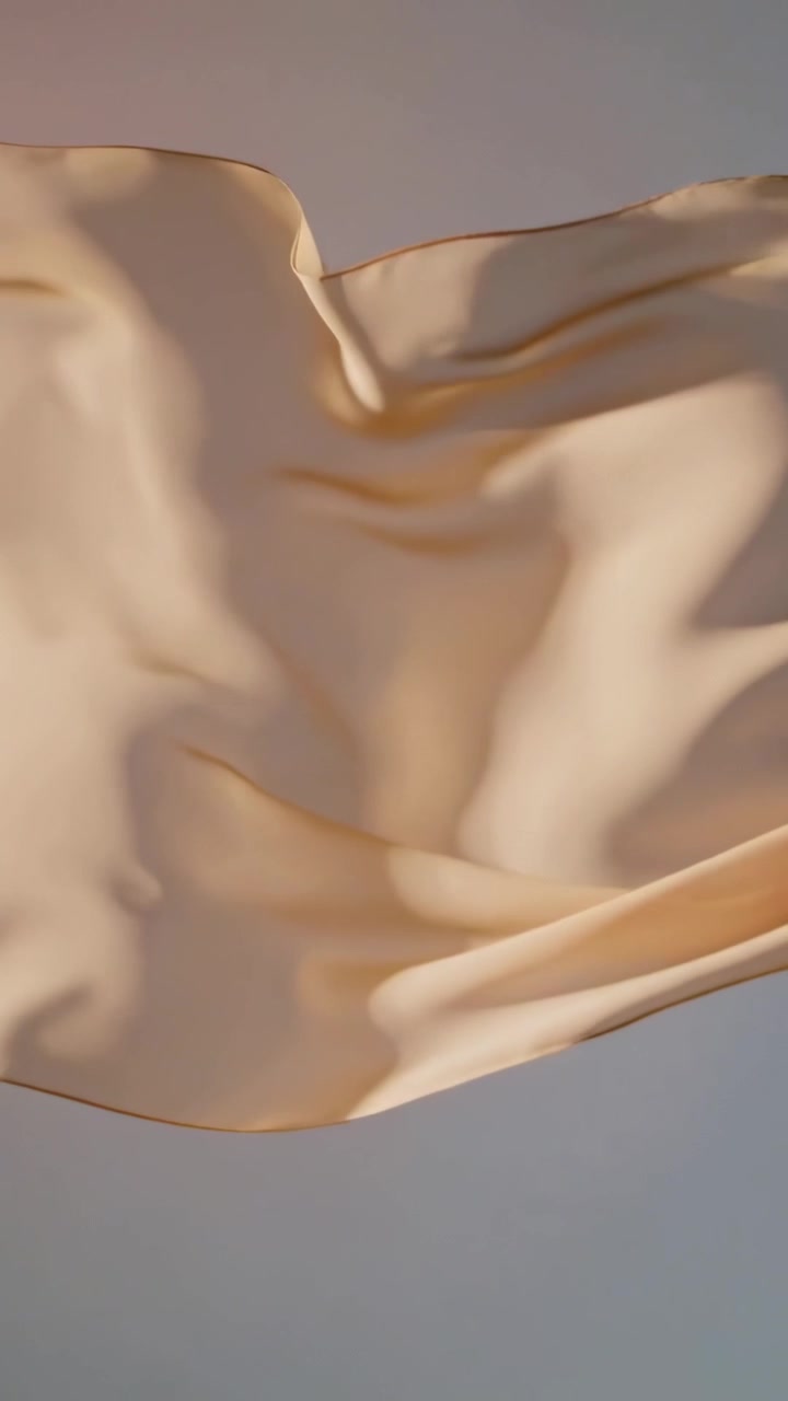 Vertical video: Floating silk twisting into folds on neutral set under lights, being pushed by fan