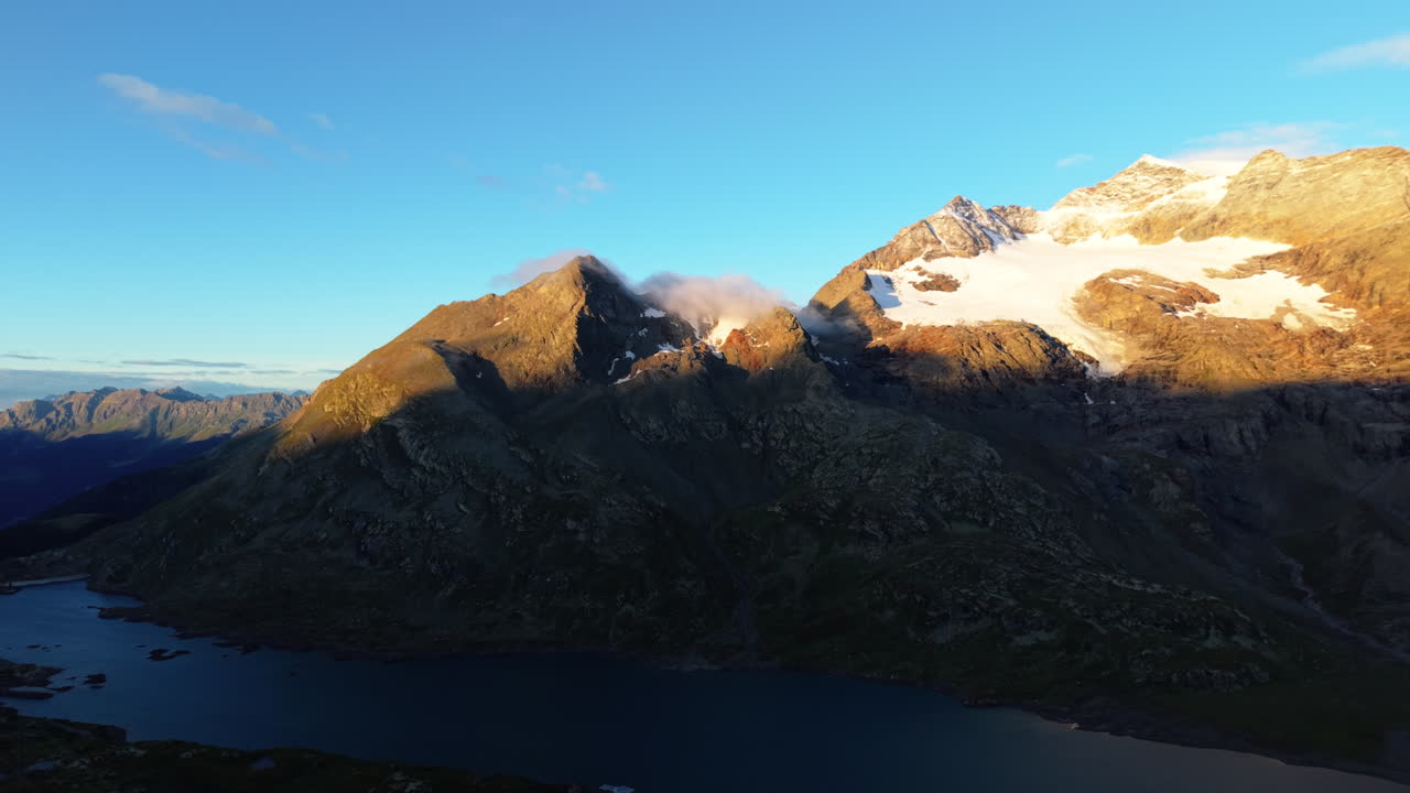 Aerial sunrise over Swiss Alps with clouds casting shadows on peaks
