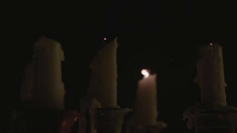 a close up of a group of melted white candles on a candelabra and all of them but one get blown out by the wind in slow motion