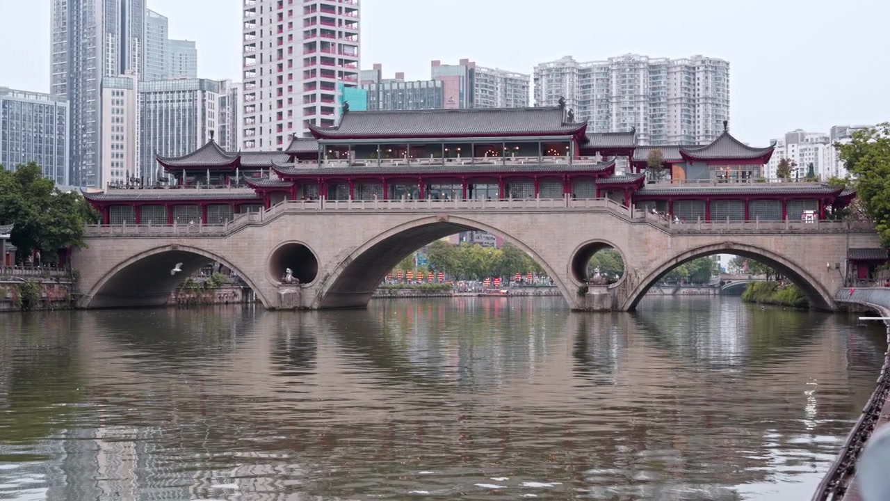 Uma ponte de pedra em arco tradicional atravessa um rio calmo, tendo como pano de fundo edifícios altos modernos. Ideal para exibir contrastes urbanos ou estudos arquitetónicos