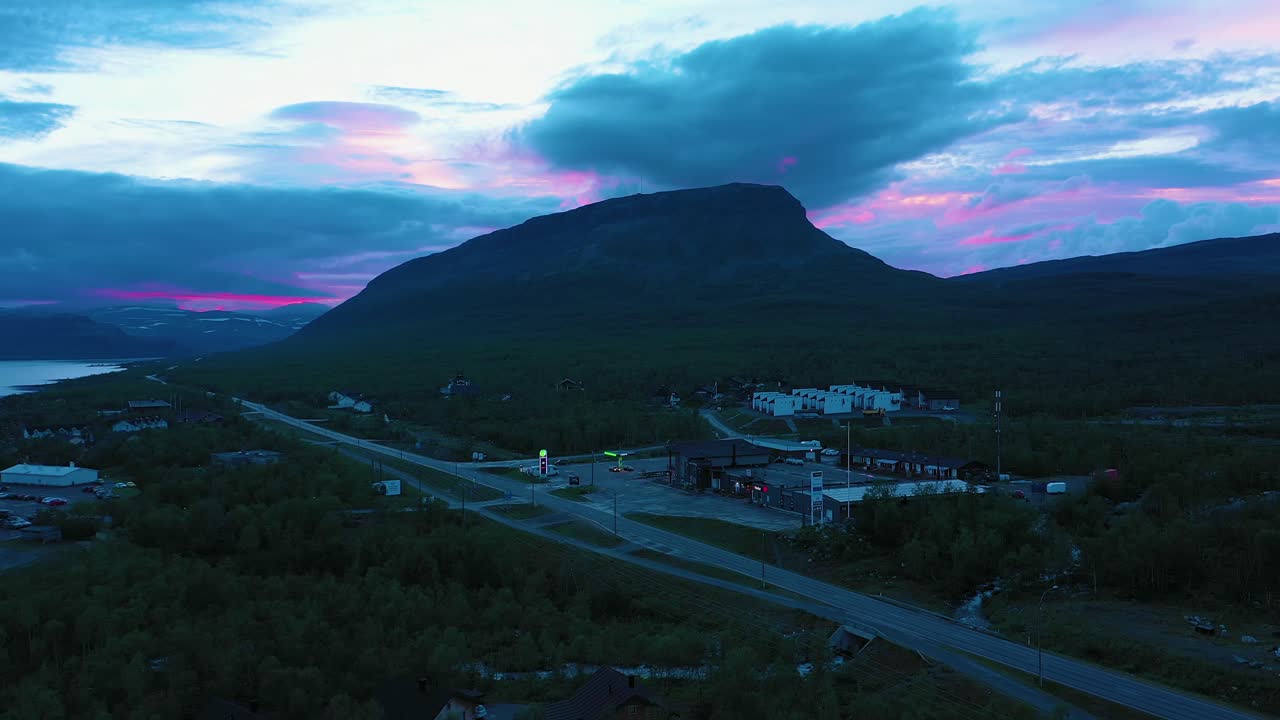 Aerial view of the Kilpisjarvi town and the Saana fell, on a colorful, gloomy, summer evening, in Kilpisjarvi, Enontekio, Lapland, Finland - rising, drone shot