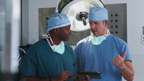 two male surgeons wearing scrubs looking at digital tablet in hospital operating theater