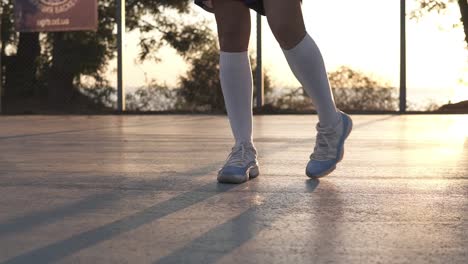 Niña-Estirando-Las-Piernas-Con-Zapatillas-Blancas-Y-Calcetines-De-Golf-Blancos-En-La-Cancha-De-Baloncesto-Local