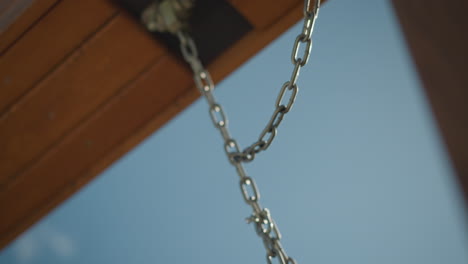 close-up of wooden swing and chain in motion under a clear bright sky, showcasing simplicity and relaxation in an outdoor setting