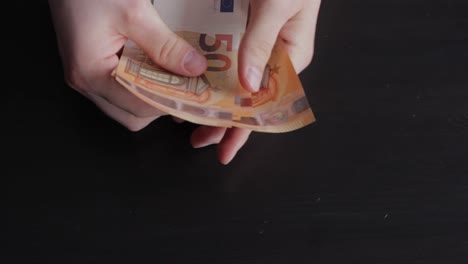 Paying-50-euros-banknotes,-hands-counting-money,-black-dark-background,-static-closeup