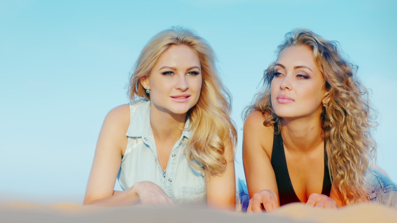 모래에 누워 해변에서 편안한 두 매력적인 섹시한 여자는 좋은 시간을 가지고