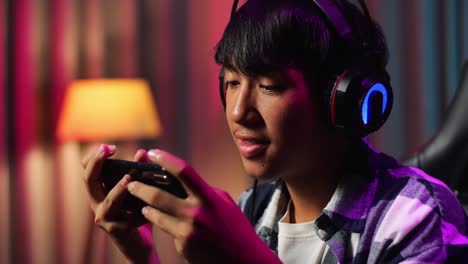close up of excited asian teen boy gamer playing video game on smartphone