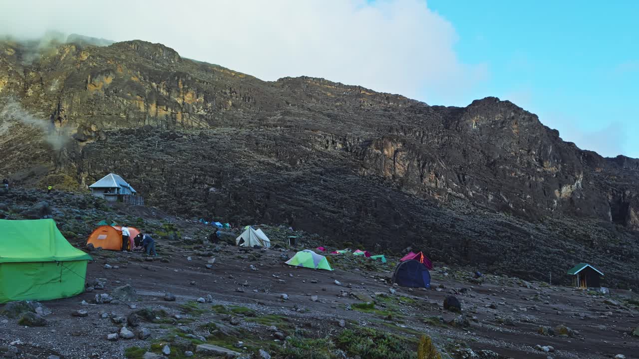 Camping tents on rocky ground at Mount Kilimanjaro base with morning light, establishing pan
