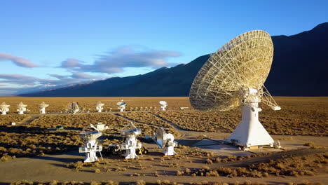 aerial drone view around a large satellite dish and multiple small desert arrays