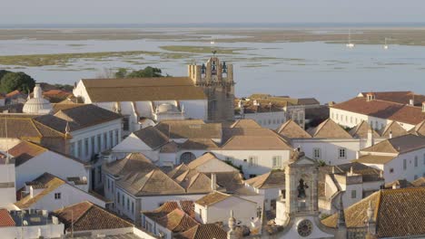 Drone-Vuela-Sobre-El-Antiguo-Pueblo-Europeo-Tradicional-En-Faro,-Portugal,-Revelando-Los-Tejados-Del-Océano-Y-El-Campanario-De-La-Iglesia,-Antena