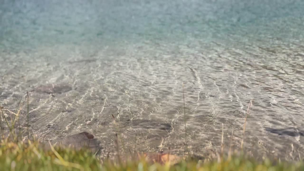 Serene lakeside with clear water, rocky shore, and peaceful sunlight reflections
