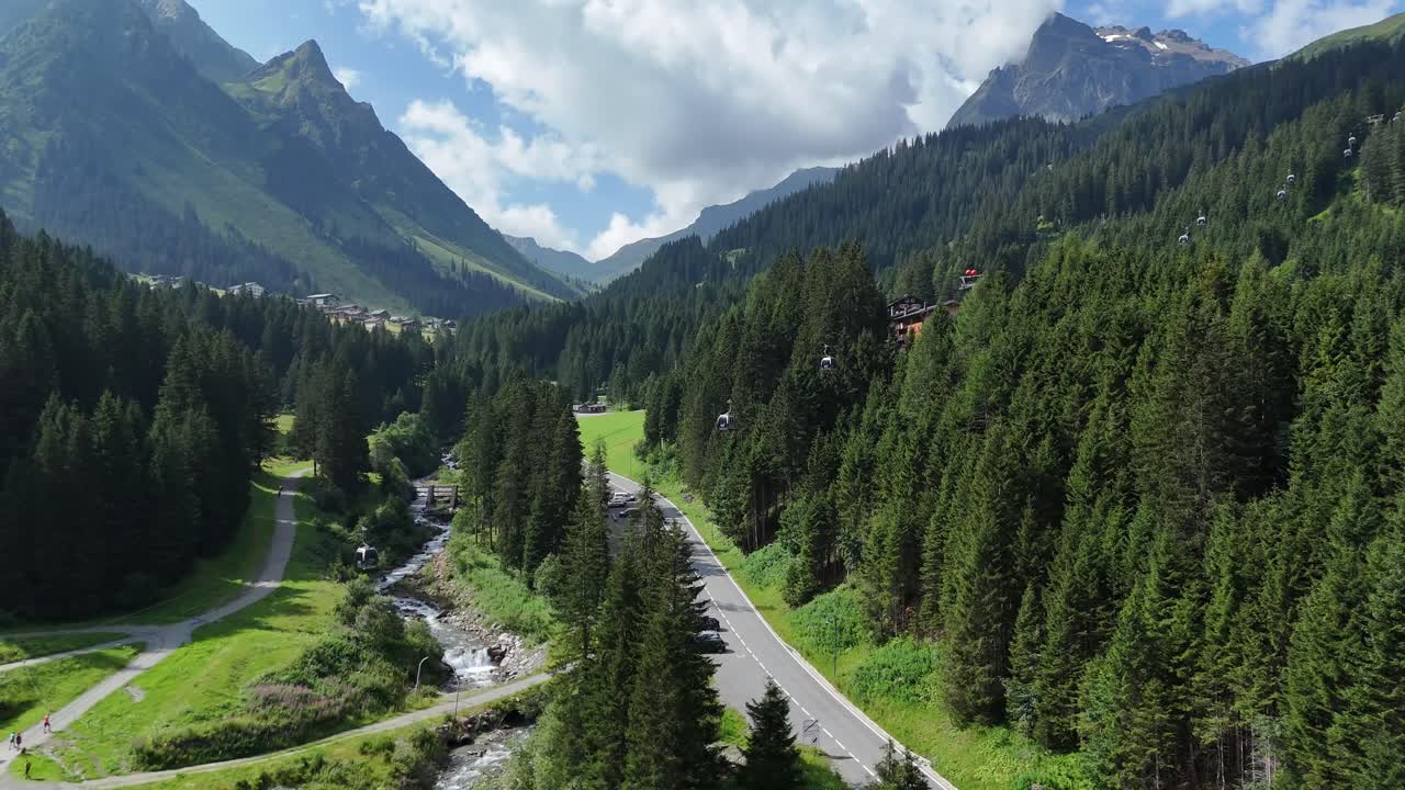 Flying over alpine region road and evergreen forest with gondola lift, Austria