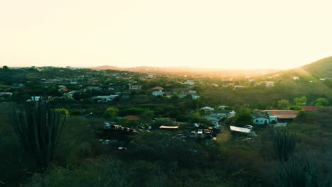 4k-aerial-of-houses-and-neighborhoods-on-the-Caribbean-island-of-Curacao,-during-golden-hour-sunset-with-flare-and-cacti-covered-hills