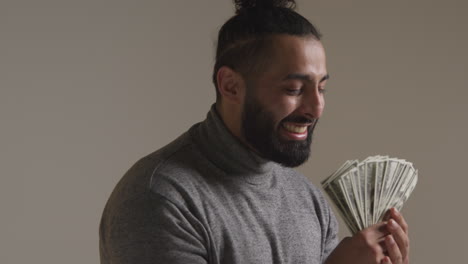 studio shot of excited young man celebrating winning cash prize holding handful of 100 dollar bills