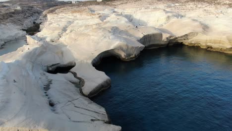 Drohnenansicht-In-Griechenland,-Die-Bei-Sonnenaufgang-über-Einem-Mondförmigen-Weißen-Felsengebiet-Auf-Der-Insel-Milos-Neben-Dem-Dunkelblauen-Meer-Fliegt