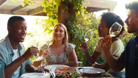 Group-Of-Smiling-Multi-Cultural-Friends-Outdoors-At-Home-Eating-Meal-And-Drinking-Wine-Together