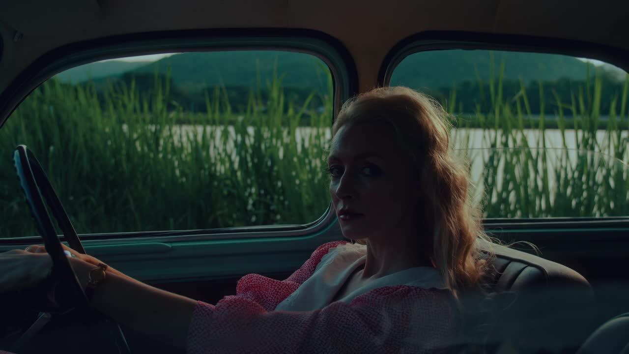 Blonde Woman Driving a Vintage Car by a River