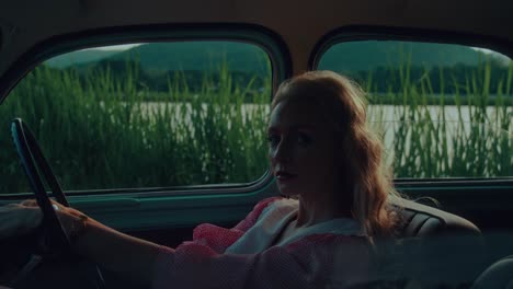 blonde woman driving a vintage car by a river
