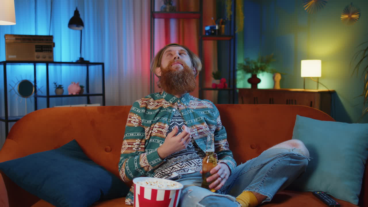 hombre sentado en el sofá lanzando comiendo palomitas de maíz y viendo series de televisión, juegos deportivos en línea en casa