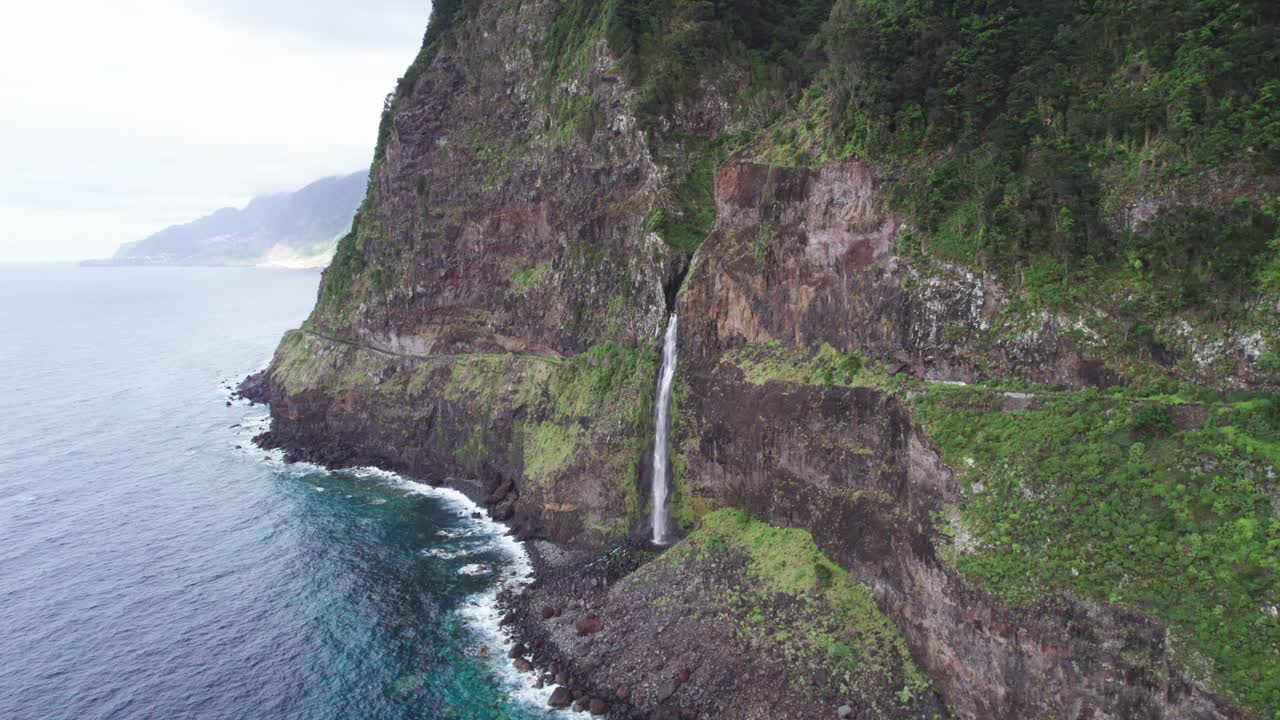 Dramatic Cascading cliffside waterfall pouring into the ocean in Madeira, Portugal with mountains in the background near Seixal village aerial drone 4k circle shot left to right