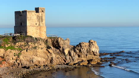 Torre-De-La-Sal-En-La-Playa-De-Casares-Manilva-En-España,-Sistema-De-Torre-Costera-Para-Vigilancia-Y-Defensa-Contra-Piratas-Bereberes,-Plantas-Verdes-En-La-Playa-Soleada,-Toma-Estática-De-4k