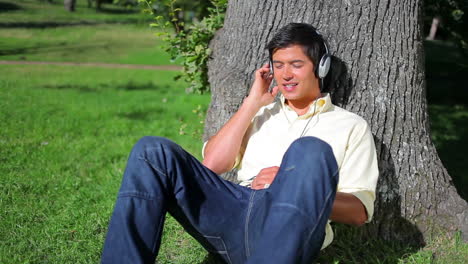 peaceful man leaning against a tree while listening to music