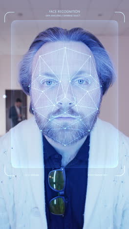 adult man scans his face in coworking office. he touches sensor and security system identifies him showing personal virtual profile. 3d hologram of human biometric facial recognition. vertical shot