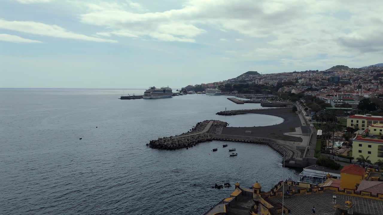 Slowmotion drone clip of Funchal coastline with visible cruise ships, old fortress, waterfront promenade and dense cityscape on Madeira island, Portugal