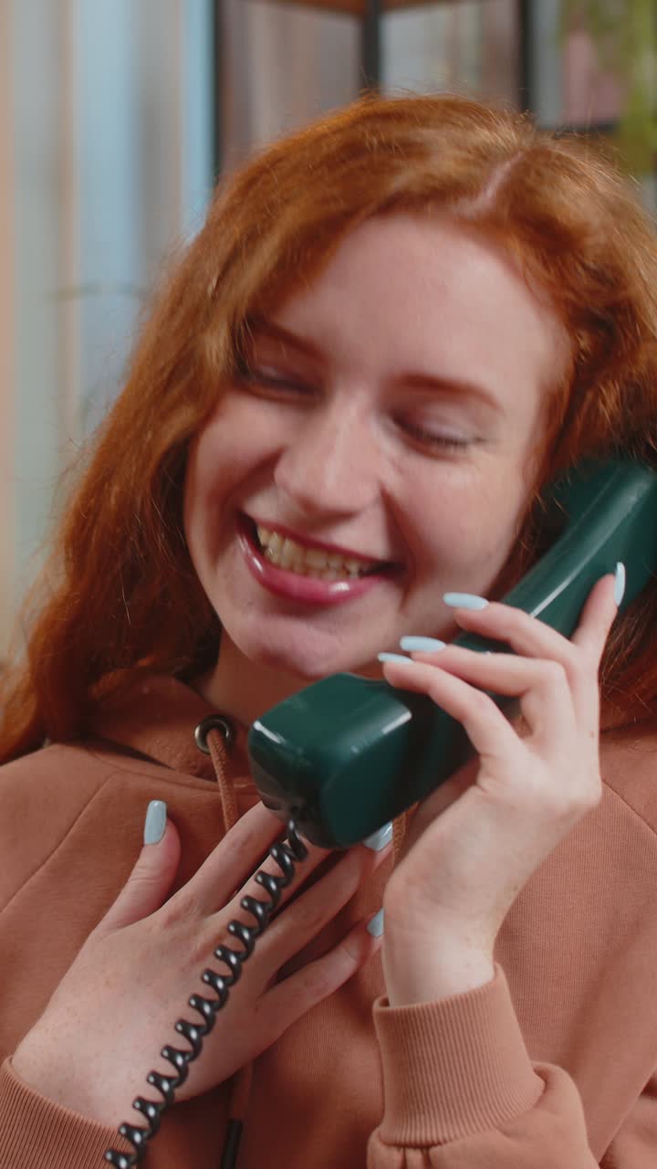 Smiling young woman making wired telephone call conversation with friends sitting on sofa at home