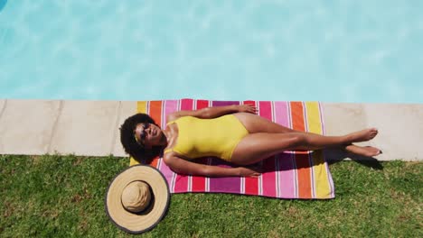 mixed race woman lying on blanket sunbathing by the pool