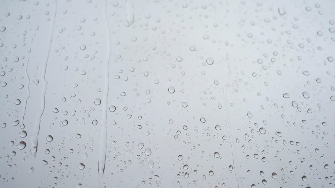 천천히 움직이는 무거운 비방울의 클로즈업 뷰가 창문 유리창을 통해 볼 수 있습니다.