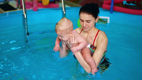 woman holding the little caucasian baby in front of her. swimming coach puts a child into water and then up.