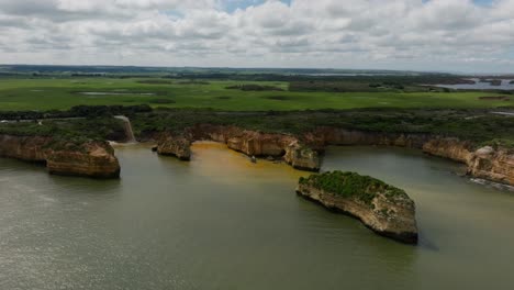 Drone-video-from-the-Great-Ocean-Road-in-Victoria-on-a-cloudy-day,-showing-off-the-orange-coloured-coastline-with-the-greenery-in-the-background