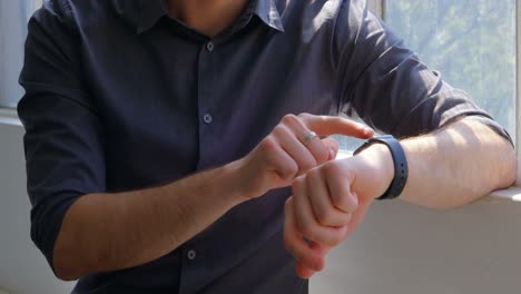 vista frontal de un joven empresario usando un reloj inteligente y sentado cerca de la ventana de una oficina moderna 4k