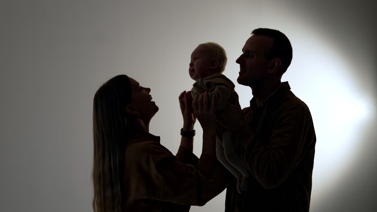 Silhouettes of young family with little baby. Mother calms down the kid crying in dad's hands.