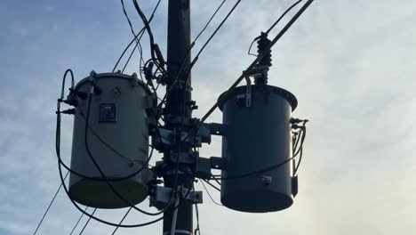 utility pole-mounted transformer system with insulated wires and metal fittings, shown against a clear daylight sky, representing energy infrastructure
