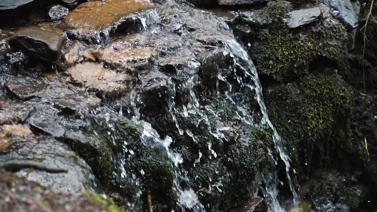 Close up of small waterfall flowing over mossy rocks in slow motion