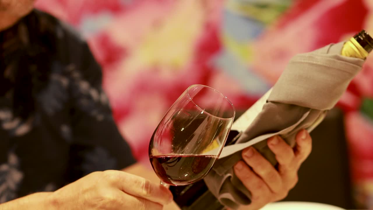 A person examines and swirls red wine in a glass, highlighting a sophisticated dining experience with warm lighting