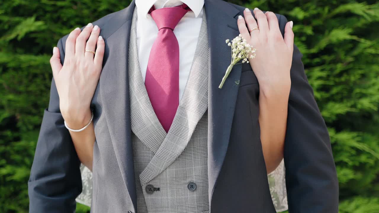 close up of bride’s hands gently placed on groom’s shoulders in wedding attire