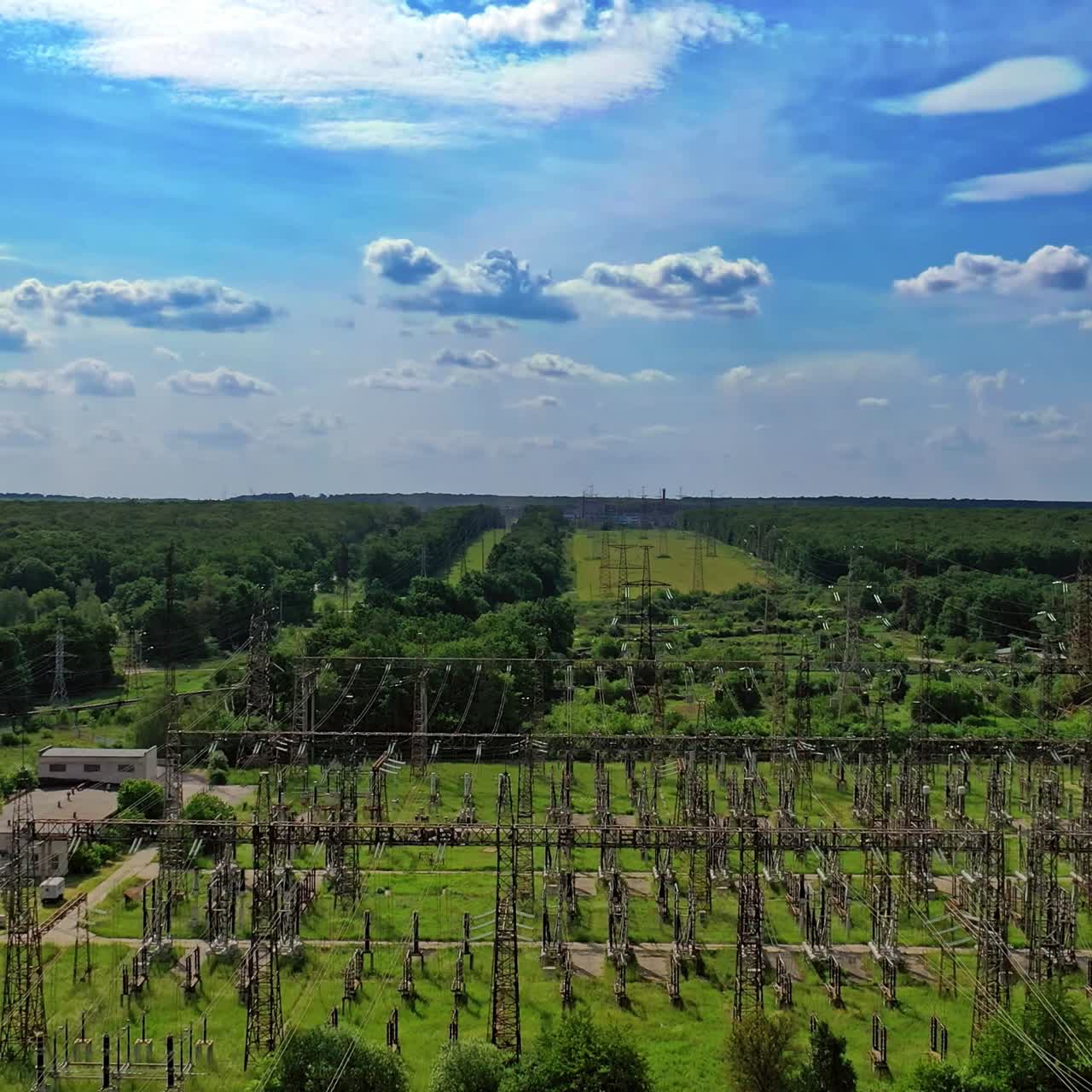 High voltage line among fields. Electric supports against the sky among green nature. Power transmission lines in summer. Aerial view.