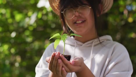 retrato de una niña asiática sosteniendo una planta en el jardín en un día soleado sonriendo
