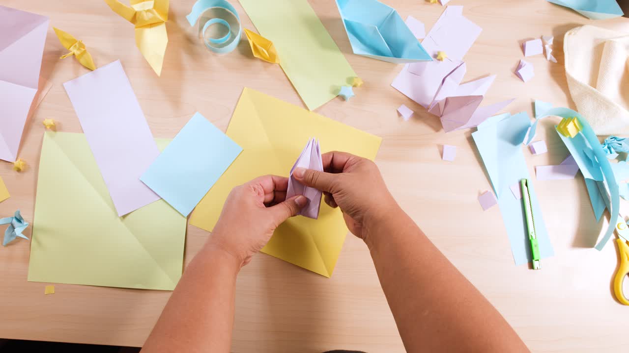 Inquadratura dall’alto di mani che piegano con cura un foglio di carta viola per creare un uccello origami su una scrivania