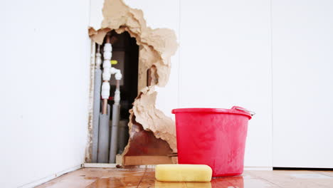 damaged wall with leaking water pipe and bucket
