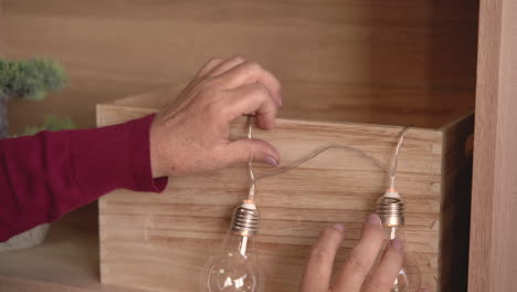 close up view of a woman's hands taking out christmas lights from a wooden box to decorate