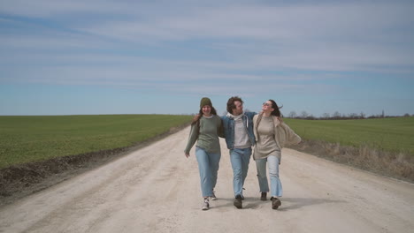 two young girls and a young boy walk happily and embraced along a road with their backs to each other