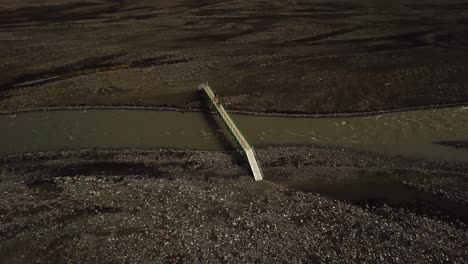 aerial panoramic view of people crossing a bridge, over a river flowing in the fimmvã¶rã°uhã¡ls area, iceland