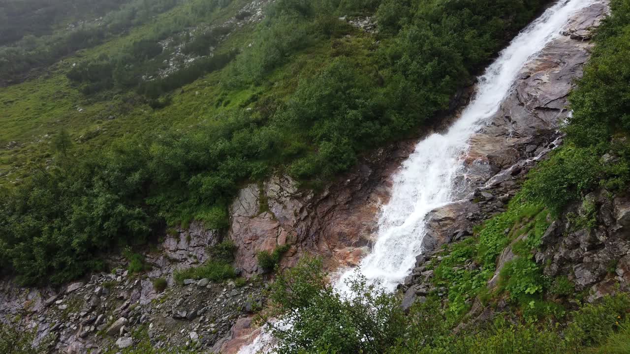 Static view of a big fast flowing alpine waterfall in rough and steep mountain terrain