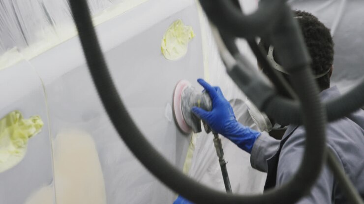 African American male car mechanic wearing a face mask and using a grinder on the side of a car